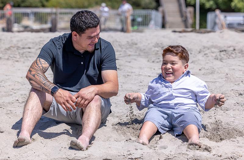 A patient and his dad sitting on the beach.